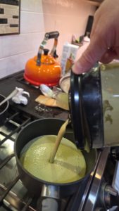 Silky Poblano cream sauce being poured from a blender into a pot to simmer at Scofield Fruits in Loveland, CO. This rich green sauce is made with fire-roasted Poblanos, candy onions, and purple garlic.